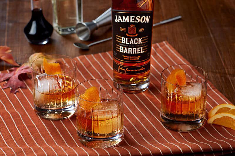 A bottle of Jameson Black Barrel on a table with 3 old fashioned cocktails